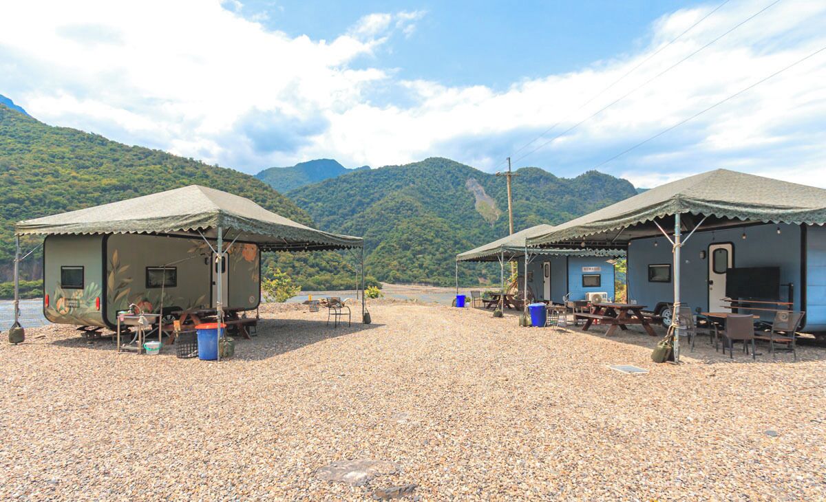 Two RV-style cabins with outdoor seating areas, a gravel ground, and a mountainous backdrop.