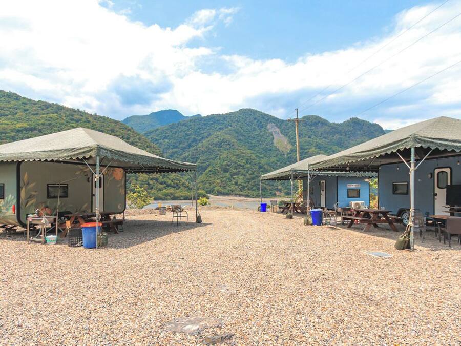 Two RV-style cabins with outdoor seating areas, a gravel ground, and a mountainous backdrop.