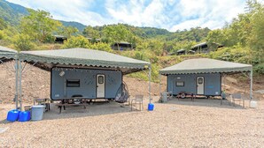 Two small, portable cabins with metal frames and corrugated roofs, set on a gravel ground with trees and hills in the background. - Tai Ping Shan Inn (Datong)