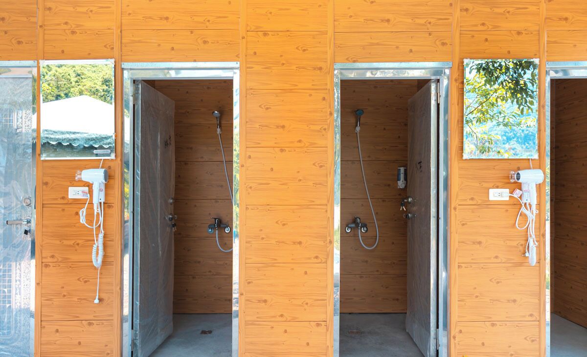 A row of wooden shower stalls with metal frames and glass doors, each with a showerhead and a towel rack.