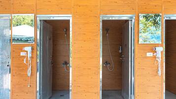A row of wooden shower stalls with metal frames and glass doors, each with a showerhead and a towel rack.