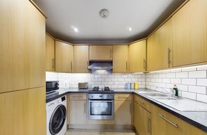 A compact kitchen with wooden cabinets, a stainless steel oven, a washing machine, and a gas stove.