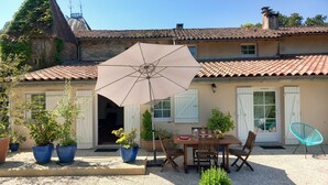 Een terras met een tafel en stoelen, een grote parasol en plantenpotten.