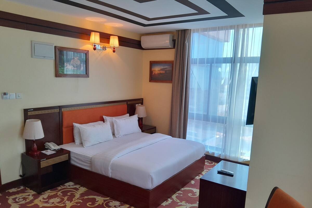 Habitación de hotel con una cama grande, dos mesitas de noche, una silla, un escritorio y una ventana con cortinas.