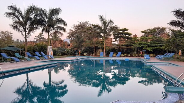 Una piscina con bordes de azulejos azules, rodeada de sillas de descanso y palmeras.