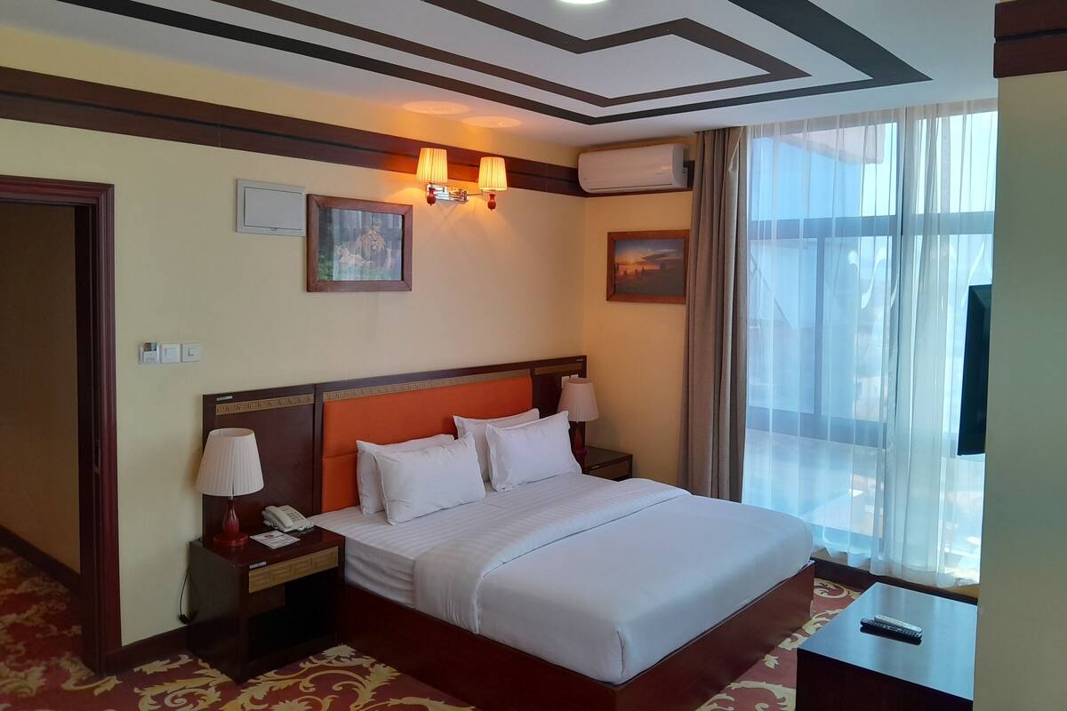 Habitación de hotel con una cama grande, lámparas de noche, mesita de noche, teléfono y una ventana con cortinas.