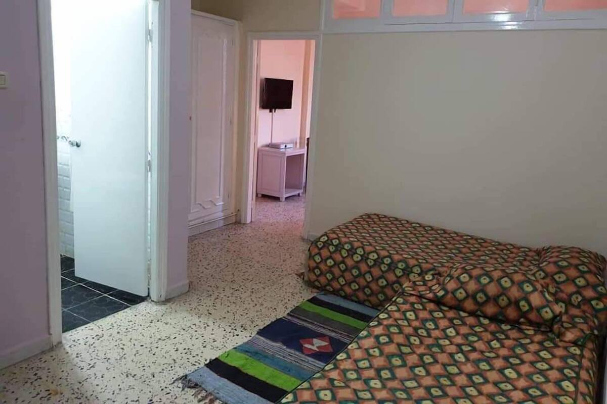 Un dormitorio con cama, un tapete estampado, una puerta y un pasillo que lleva a otra habitación.