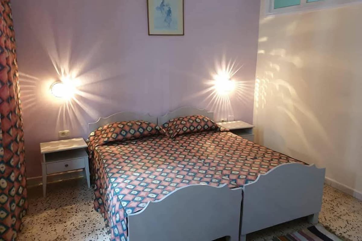 A bedroom with a bed, two bedside lamps, a nightstand, a wall-mounted picture, and a window.