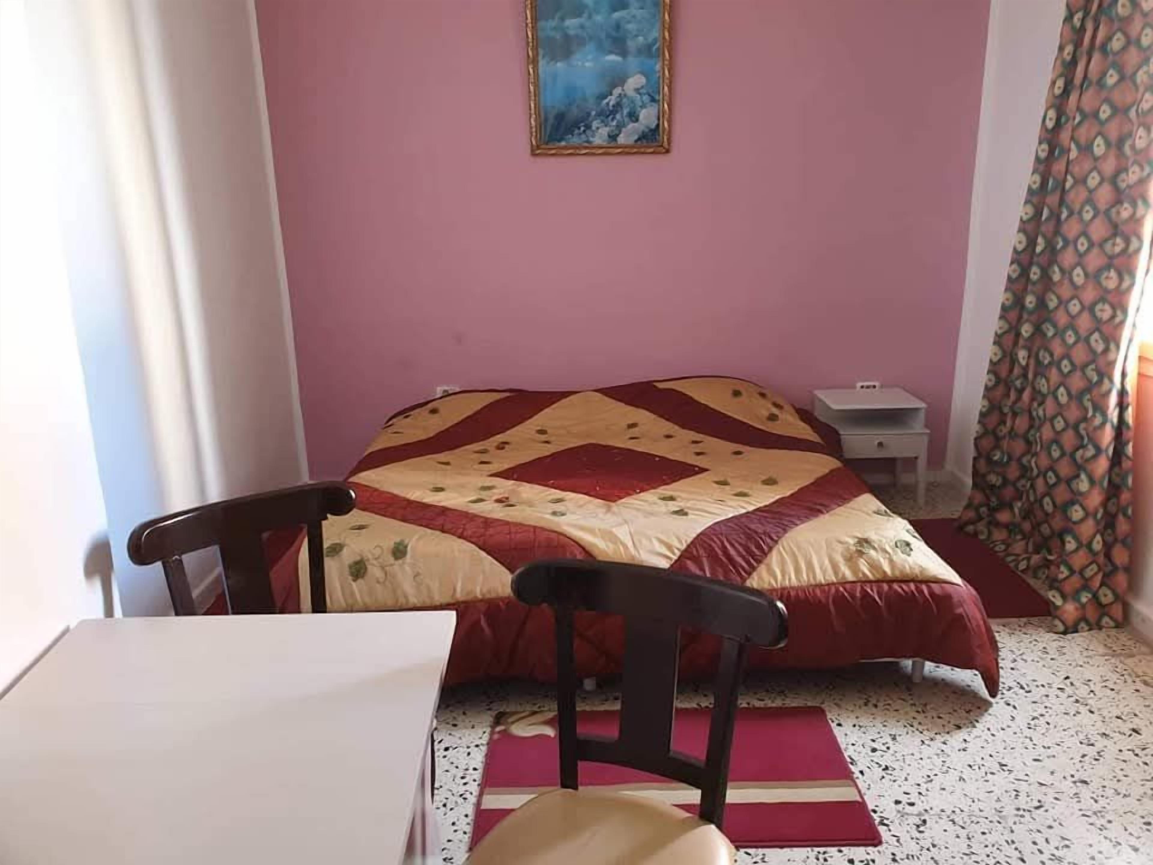 Una camera da letto con un letto, una sedia, un comodino e un quadro appeso al muro.