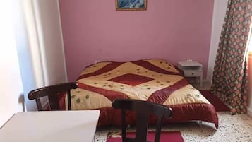 Una camera da letto con un letto, una sedia, un comodino e un quadro appeso al muro.