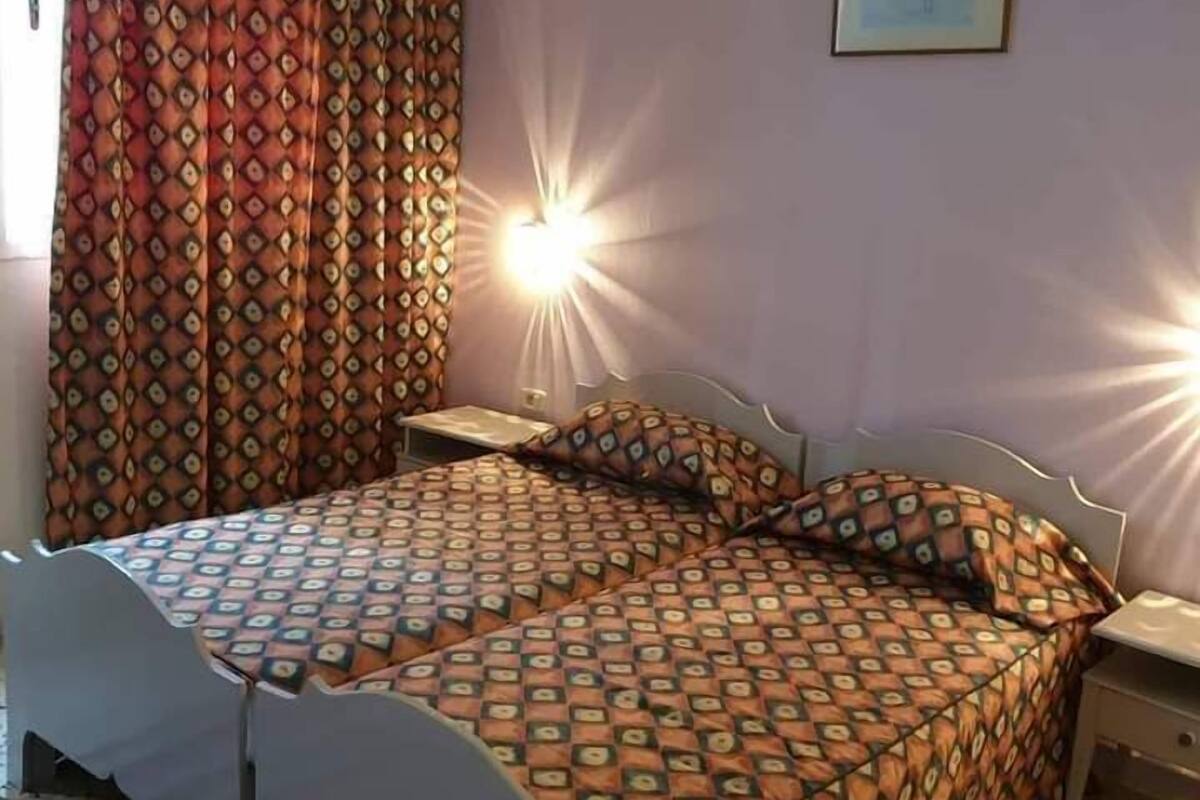 Un dormitorio con cama, cortinas, una mesita de noche y un cuadro colgado en la pared.