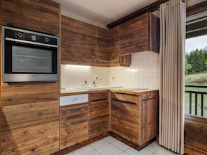 A kitchen with wooden cabinetry, a built-in oven, and a window with curtains.