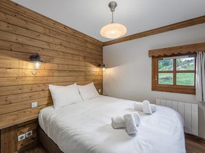 A wooden-paneled room with a bed, two wall-mounted lights, a window with a view, and a ceiling light.
