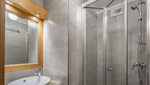 Un bagno con un lavandino grande e bianco, un piano d'appoggio in legno, uno specchio e una cabina doccia in vetro con soffione a mano.