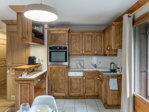 Une cuisine dotée de meubles en bois, d’un four encastré, d’un évier et d’un coin repas avec une table et des chaises.