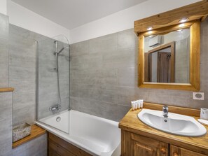 A modern bathroom with a glass-enclosed shower, a wooden vanity with a sink, and a large mirror.