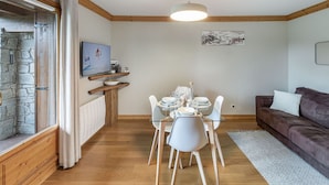 Un soggiorno moderno con zona pranzo, parete in pietra, travi in legno e televisore a parete.