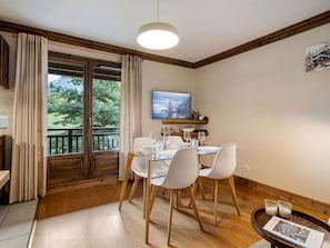 A dining area with a table set for four, a television mounted on the wall, and a view of a mountainous landscape through the window.