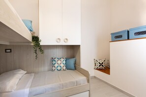 Une chambre à coucher de taille réduite, équipée d’un lit superposé, d’un petit bureau et d’une étagère avec des boîtes de rangement.