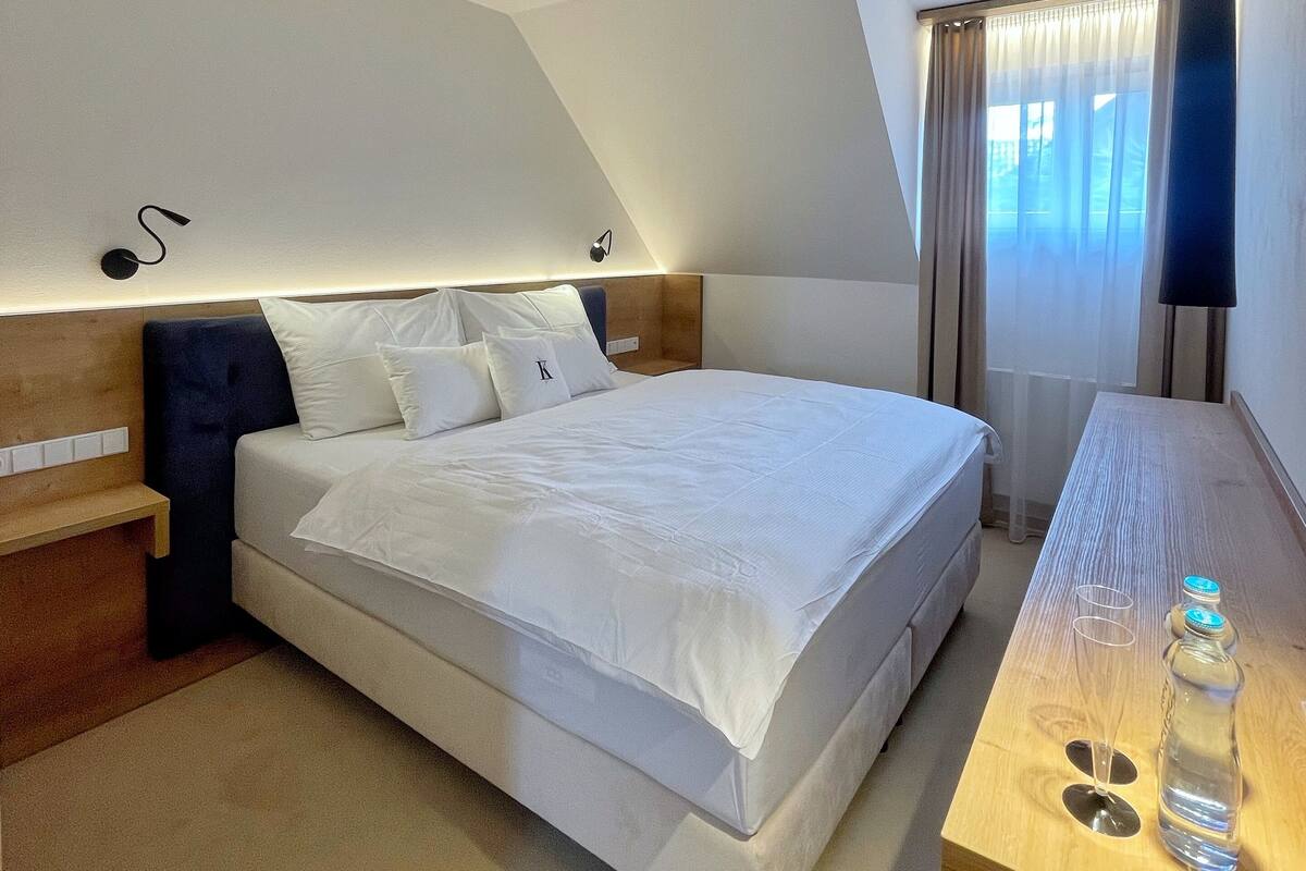 Een moderne hotelkamer met een groot bed, nachtkastjes, een bureau met lamp en een raam met gordijnen.