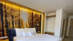 A modern hotel room with a large bed, a wall-mounted TV, and a built-in bookshelf. - Wellness penzion Lázně Kvilda (Kvilda)