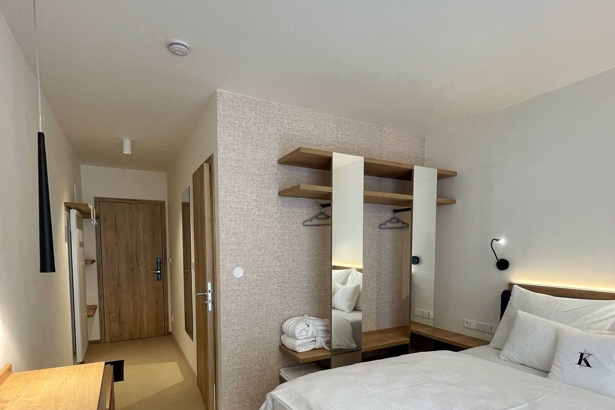 Een hotelkamer met een groot bed, een houten bureau, een kledingkast met ophanging en een spiegel.