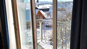 A room with a large sliding glass door leading to a balcony. The balcony has a metal railing and a view of a snowy landscape with buildings in the distance. - Wellness penzion Lázně Kvilda (Kvilda)