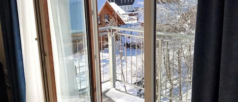 A room with a large sliding glass door leading to a balcony. The balcony has a metal railing and a view of a snowy landscape with buildings in the distance.