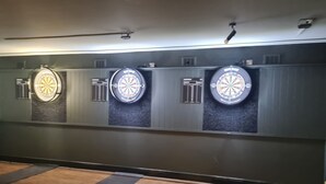 A dartboard wall with three dartboards, a wooden floor, and a black mat with measurements. - The Hen House (Cannock)