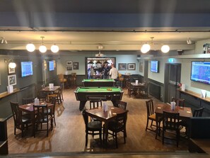 A billiards room with tables, chairs, and a pool table. There are multiple screens displaying content. - The Hen House (Cannock)