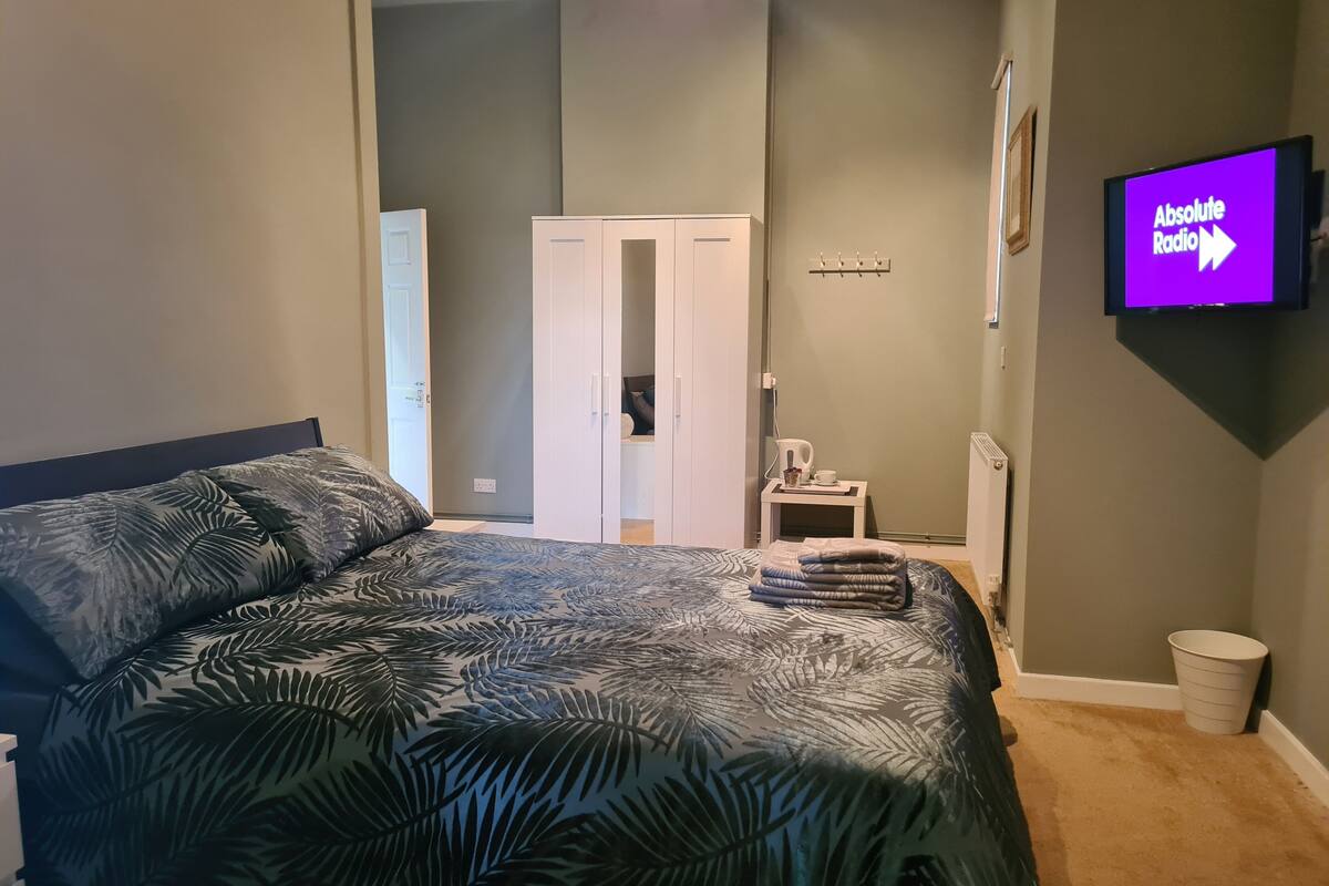 Quarto com cama, guarda-roupa, televisão e uma pequena mesa com chaleira e ch ávena.