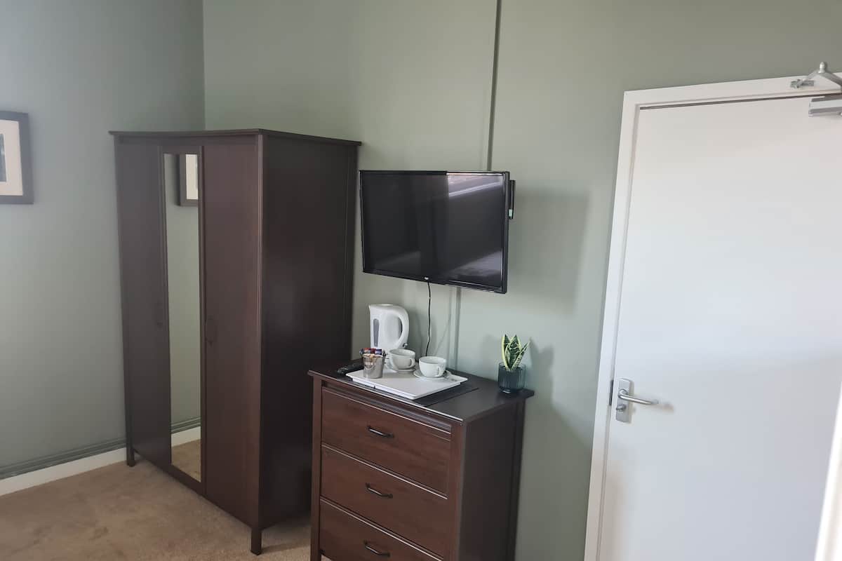 Quarto com guarda-roupa de madeira escura, escrivaninha com TV de tela plana, chaleira e uma pequena planta.