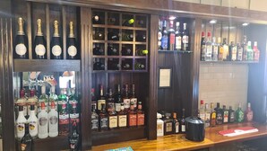 A bar area with various liquor bottles, including vodka, whiskey, and gin, arranged on shelves and the counter. - The Hen House (Cannock)