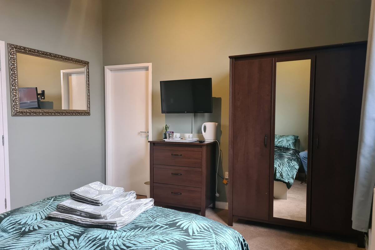 Um quarto com uma cama, cômoda, televisão e guarda-roupa.