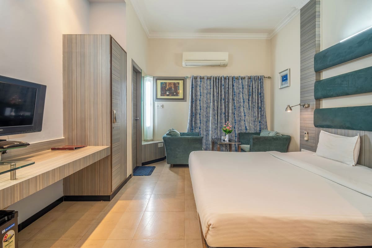 Habitación de hotel con cama, televisión, escritorio, sofá y una mesita con un florero.
