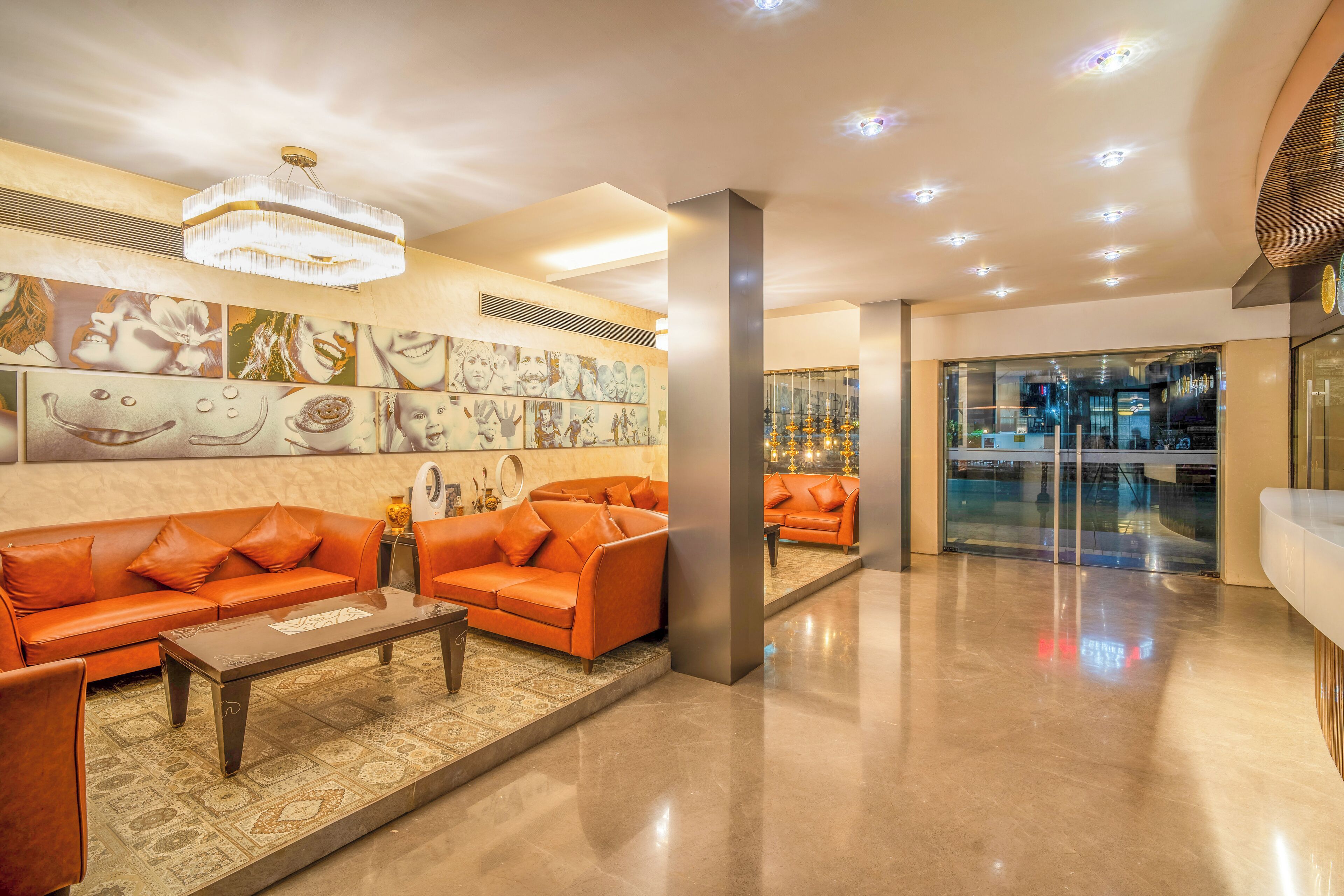 Un hall d’entrée moderne avec des canapés orange, un lustre et des œuvres d’art accrochées aux murs.