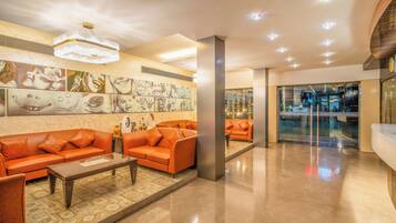 Un hall d’entrée moderne avec des canapés orange, un lustre et des œuvres d’art accrochées aux murs.