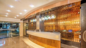 Un área de recepción moderna con un mostrador curvo, puertas de cristal y una pared decorativa con líneas verticales.