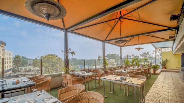 Un área de comedor al aire libre con mesas y sillas, vistas de la ciudad y una sección cubierta con ventilador de techo.