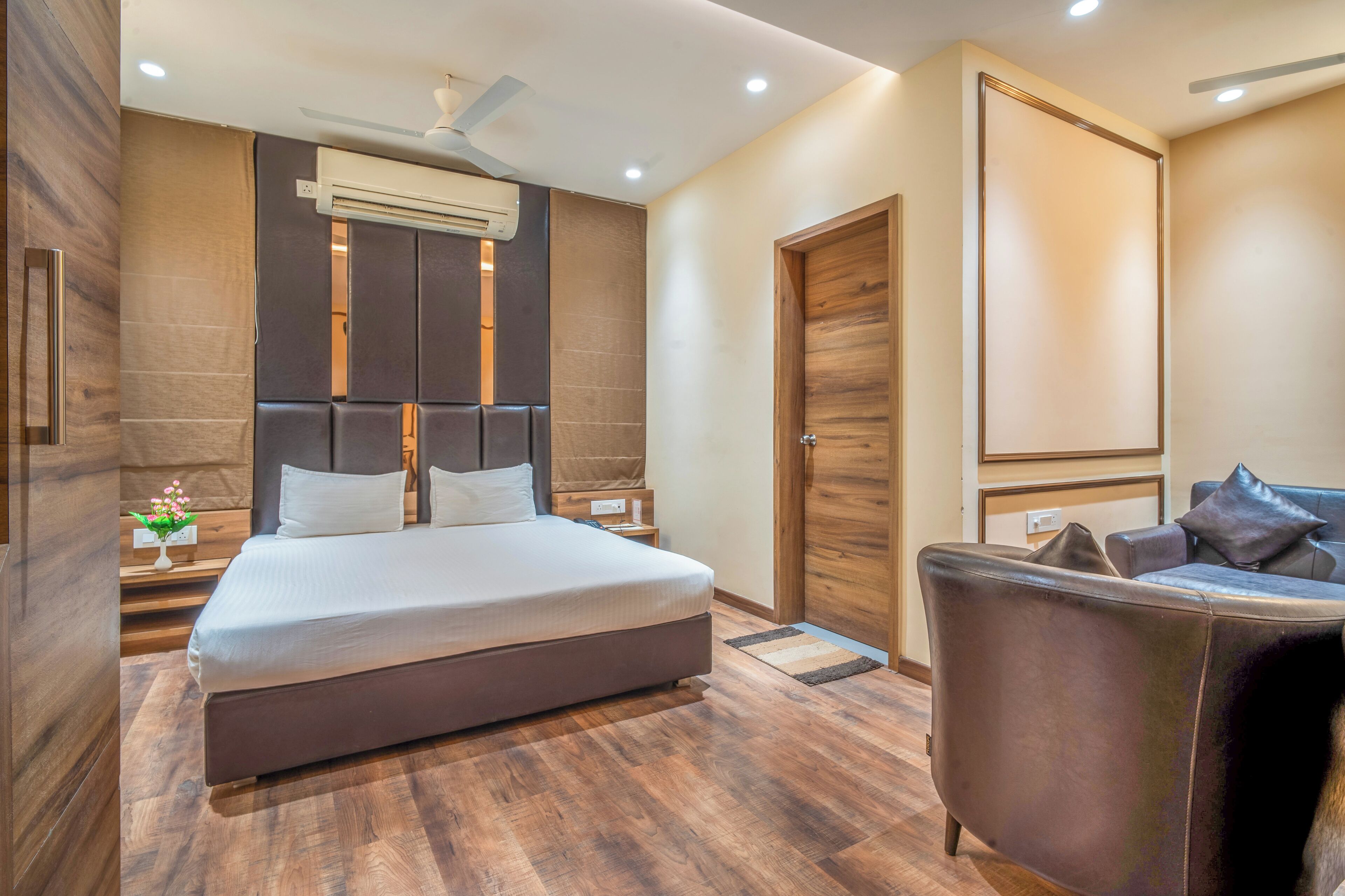 A modern bedroom with a large bed, a wooden headboard, a nightstand, a sofa, and a wardrobe.