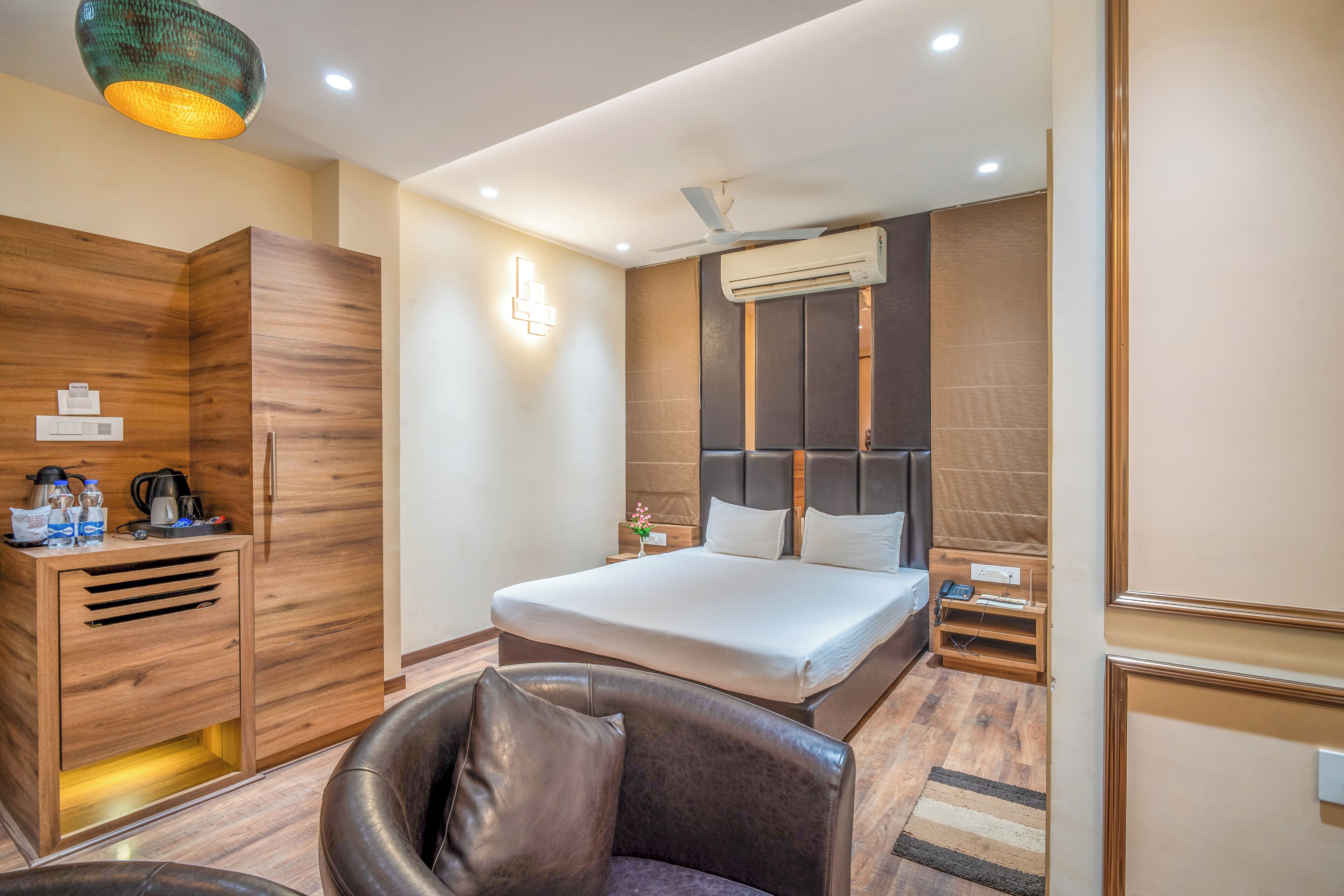 A hotel room with a bed, a wooden wardrobe, a desk with a lamp, and a chair.