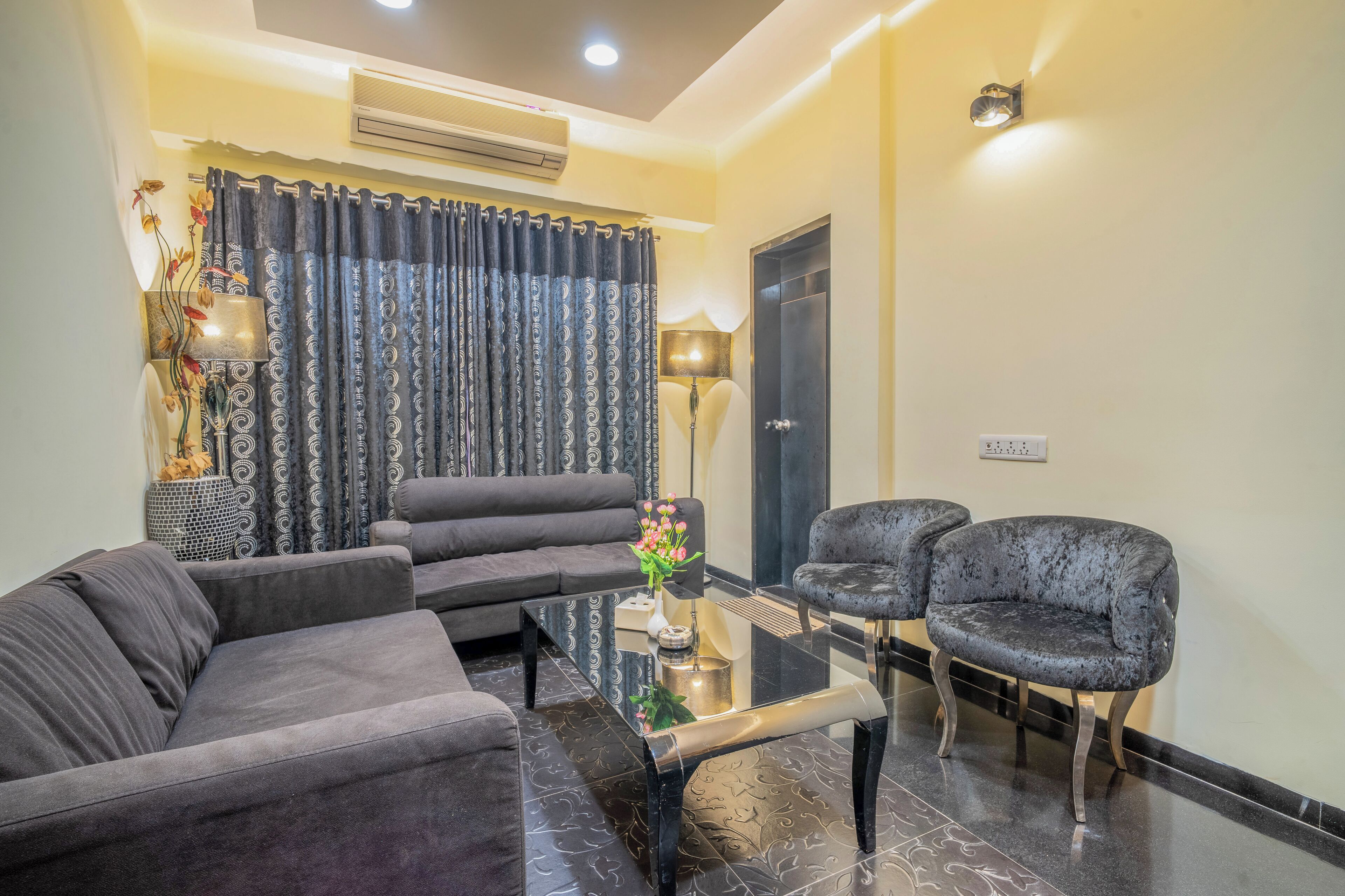 Una sala de estar moderna con un sofá, dos sillones, una mesa de centro de vidrio y un jarrón decorativo con flores.