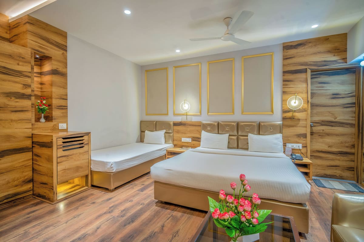 Habitación de hotel con una cama grande, dos camas individuales, paneles de madera, ventilador de techo, lámparas de noche y un florero con flores.