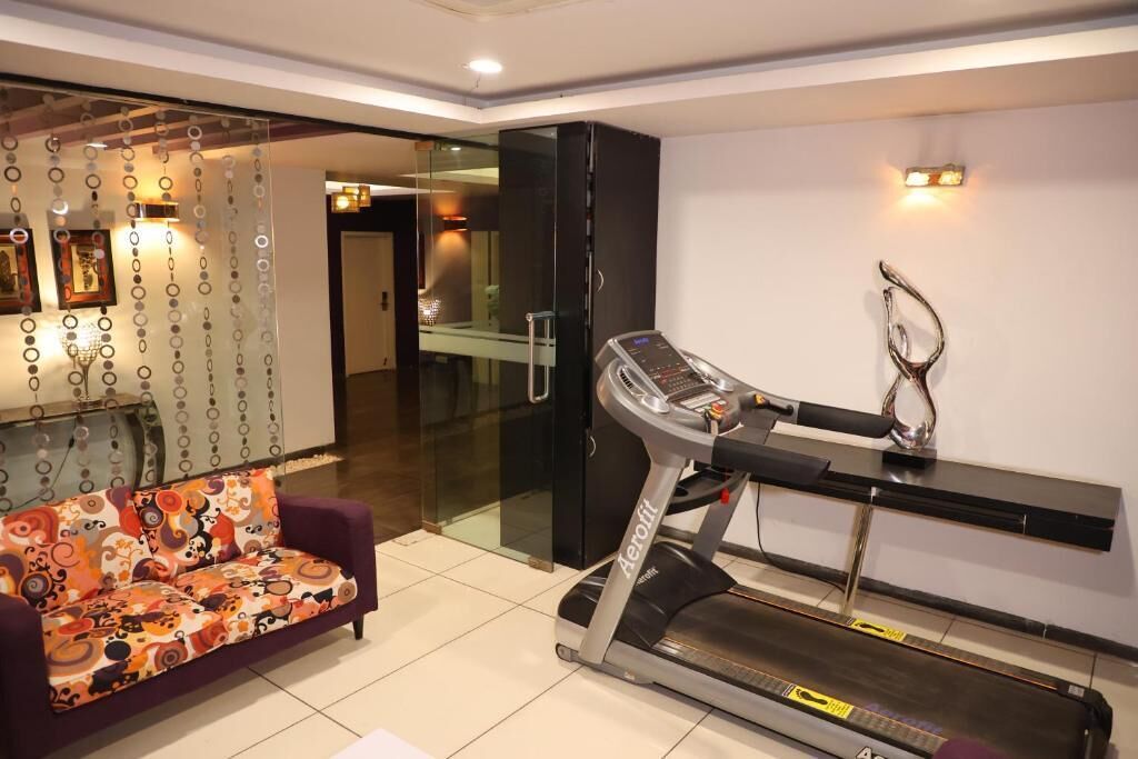 Una habitación moderna con una cinta de correr, un sofá estampado y un separador de vidrio.