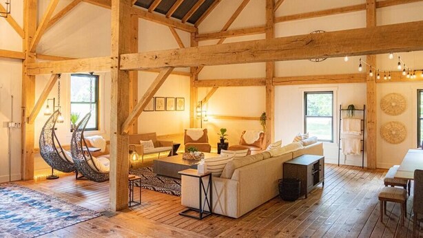 Ett rymligt loft med synliga träbjälkar, en stor soffa, hängstolar och en matplats.