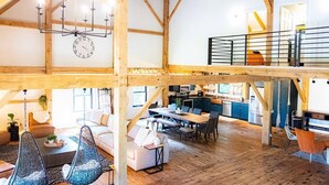 En rymlig interiör i loftstil med synliga träbjälkar, ett matområde och ett kök.