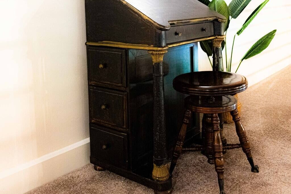 Un bureau d’angle avec un tiroir, un petit tabouret et une plante.