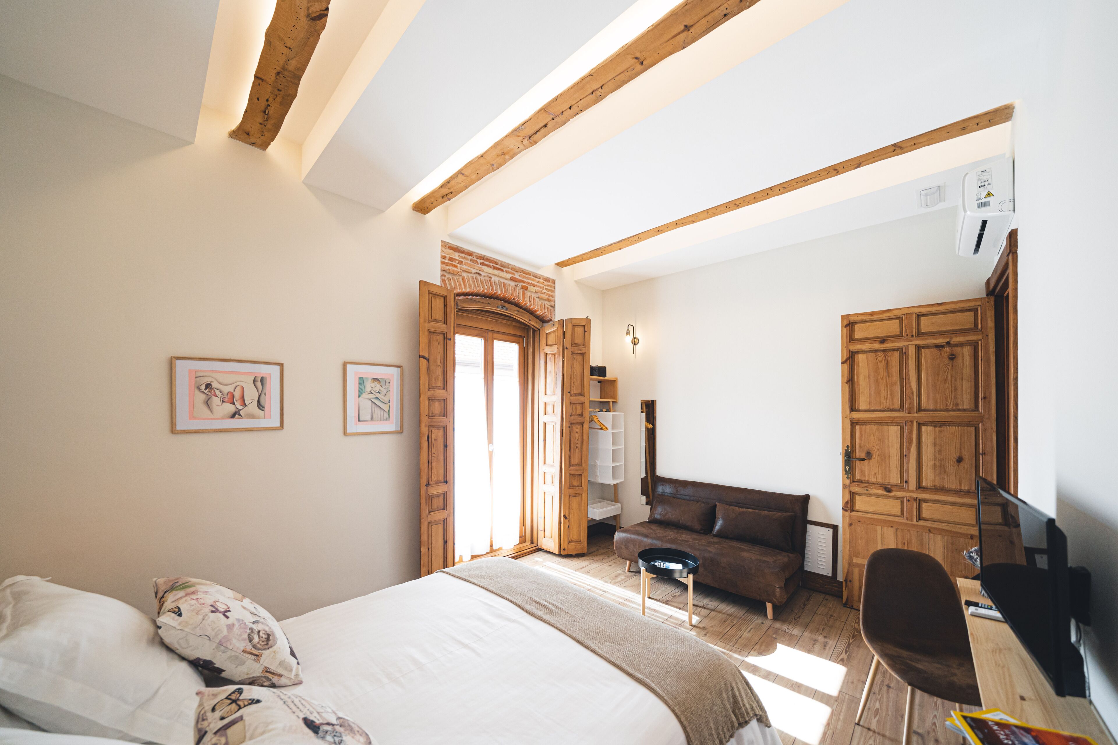 A bedroom with a bed, a desk, a chair, a wardrobe, and a door leading to another room.