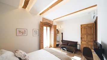 A bedroom with a bed, a desk, a chair, a wardrobe, and a door leading to another room.