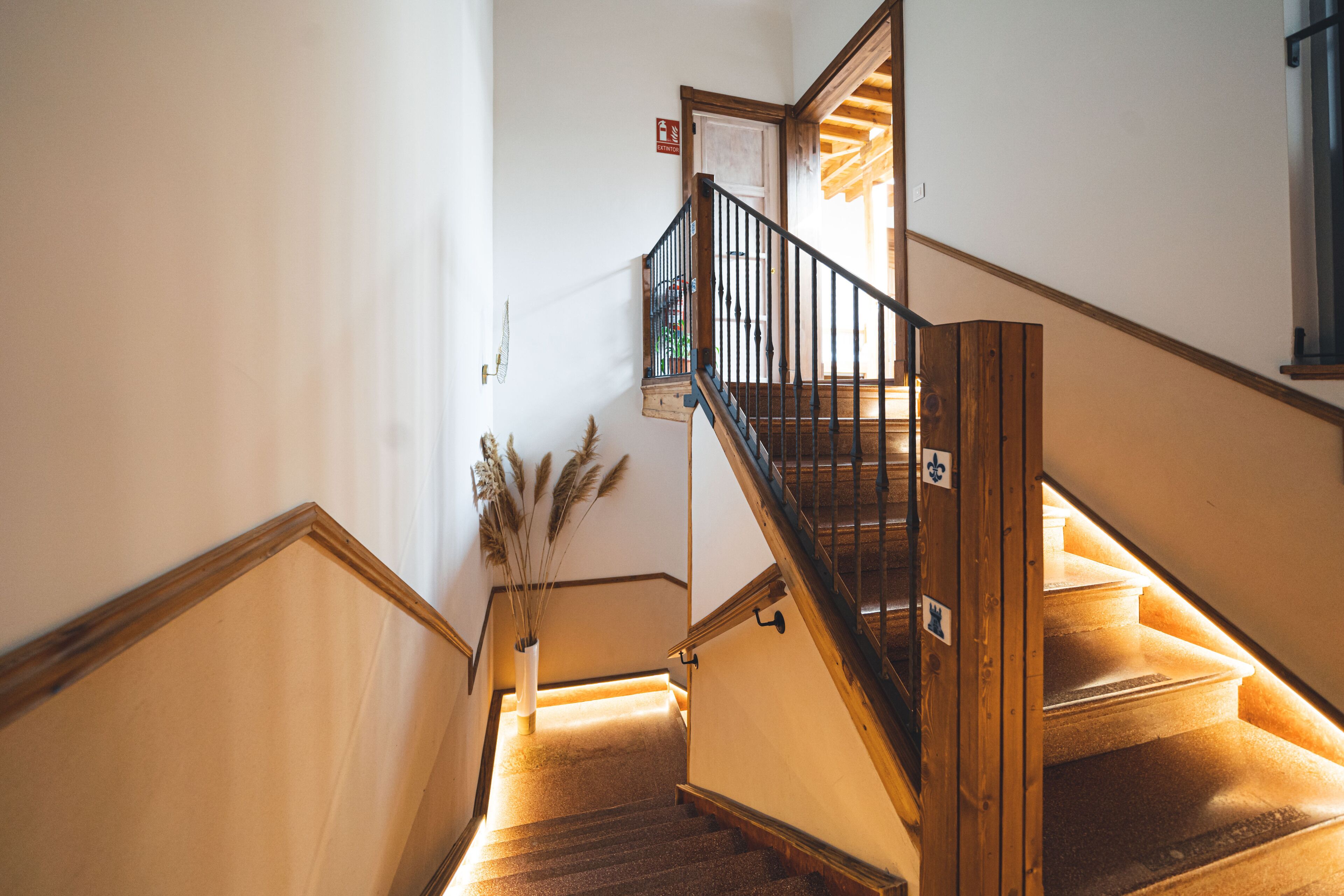 Una escalera de madera con barandilla, un jarrón con plumas de plumero y una puerta con un letrero.